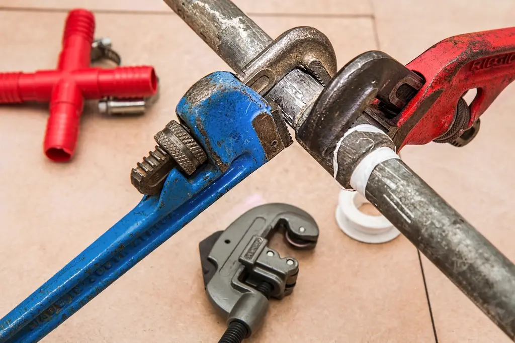 Pipe wrenches gripping a pipe on a tile floor
